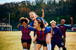 Excited teammates celebrate victory during women's soccer match on playing field.