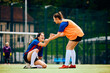 Happy female player helps her teammate to get up on soccer pitch.