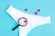 heart lies under a magnifying glass of women's panties, among many other hearts on light blue background. concept of searching for lover, find lover. Love background. romantic minimalism background. 