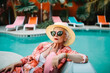 Fashionable, rich, elderly woman relaxing near the pool in a hat and jewelry.