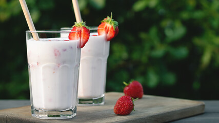 Wall Mural - Strawberry smoothie in two glass glasses and fresh strawberries on a wooden table in the yard, copyspace