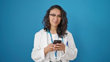 Sticker - Young beautiful hispanic woman doctor smiling using smartphone over isolated blue wall background