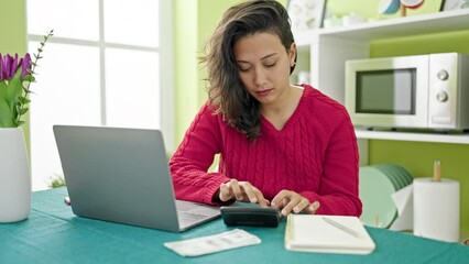 Canvas Print - Young beautiful hispanic woman using laptop counting dollars at dinning room