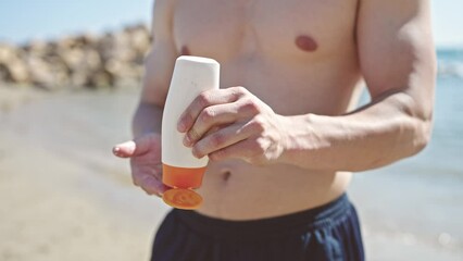 Sticker - Young hispanic man tourist applying sunscreen on arm at seaside