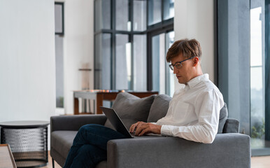 businessman typing in laptop sitting on sofa in modern apartment