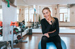 © Iona - Cheerful caucasian young woman in black sportswear sitting on fit ball at fitness club toothy smiles looks away dreamily satisfied by great training. Smiley American girl at break of exercise. Fitness