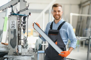 Wall Mural - Portrait of factory worker in protective uniform and hardhat standing by industrial machine at production line. People working in industry