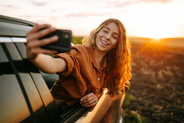 Wall Mural - Selfie time. Young woman takes a selfie in the car during a road trip. Lifestyle, travel, tourism, nature, active life.