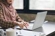 Cropped shot of Muslim millennial Asian businesswoman wearing a brown hijab hands using laptop computer working remotely from her home office.