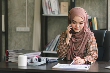 Wall Mural - A confident,beautiful, professional, millennial Muslim Asian businesswoman wearing a brown hijab is working remotely from modern office.