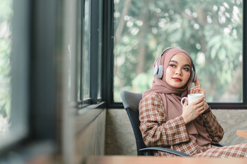 Wall Mural - A confident,beautiful, professional, millennial Muslim Asian businesswoman wearing a brown hijab is relaxing in her office and having coffee.