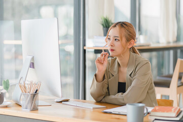 A focused and professional millennial Asian graphic designer, woman working on computer and deep in thought at modern office.