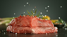 Close-up Of Falling Salt And Pepper On Raw Beef Steaks.
