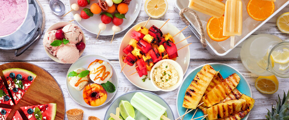 Wall Mural - Refreshing summer food table scene. Mixture of grilled fruits, ice cream and ice pops. Above view on a white wood banner background.