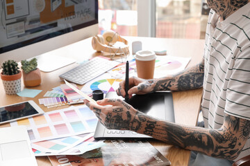 Wall Mural - Tattooed graphic designer working with tablet and paint palette on table in office, closeup