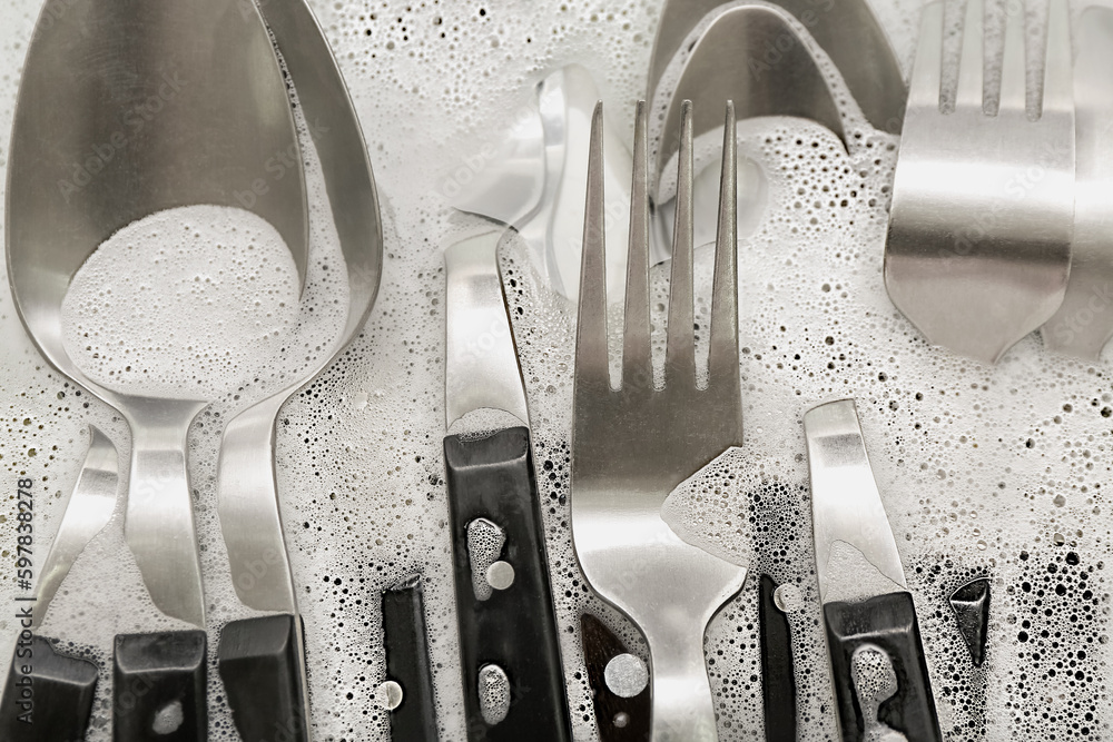 Silver cutlery with foam in water, closeup