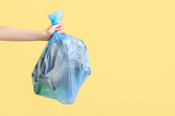 Female hand holding full garbage bag on yellow background