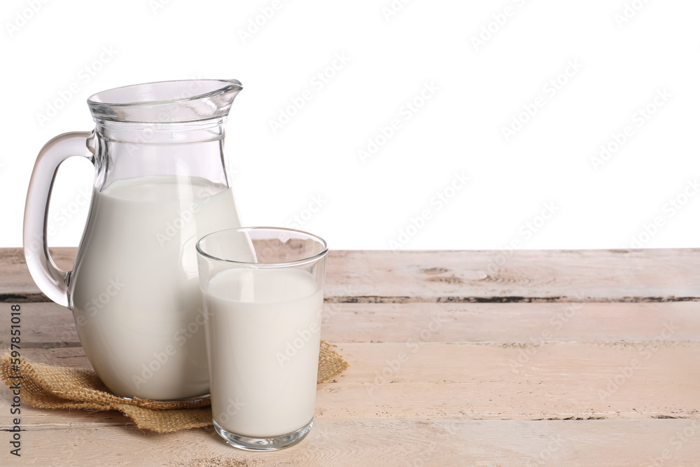 Jug and glass of milk on table against white background