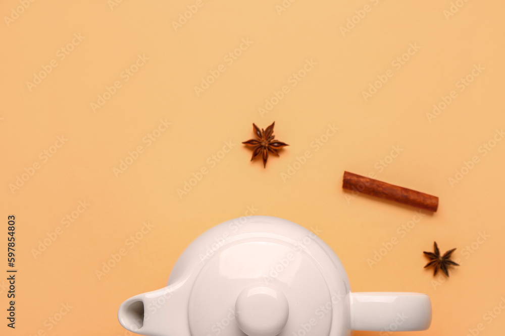 Ceramic teapot with spices on orange background