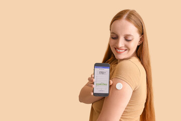 Woman with glucose sensor using mobile phone for measuring blood sugar level on beige background