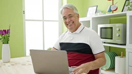 Poster - Middle age man with grey hair using laptop sitting on table at dinning room