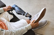 © insta_photos - Man amputee with prosthetic leg disability on above knee transfemoral leg prosthesis wearing shoe sitting on sofa, close up. People with amputation disabilities everyday life concept.