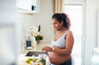 © Baba Images - Young pregnant latina woman preparing a salad in the kitchen