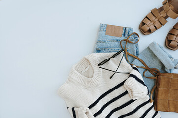 Aesthetic casual fashion composition with female clothes and accessories. Striped sweater, leather sandals, suede bag, jeans, sunglasses. Flat lay, top view.