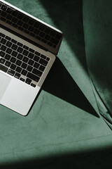 Wall Mural - flatlay laptop computer and gentle sunlight shadow on green velour sofa. top view minimalist aesthet