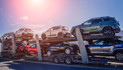 car carrier trailer transports cars on highway at blue sky background.