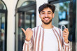 © luismolinero - Handsome Arab man holding invisible braces at outdoors pointing to the side to present a product