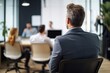 © Road Red Runner - A professional businessman attentively listens to a colleague's presentation, his back turned to the camera, surrounded by modern office. Ai generated.