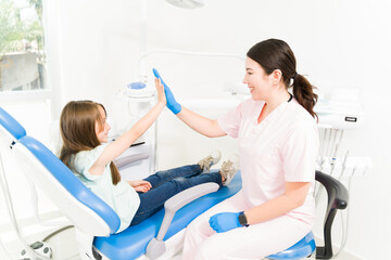 Wall Mural - Happy female pediatric dentist celebrating with a kid patient