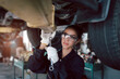 © Stella - Beautiful female auto mechanic checking wheel tires in garage, car service technician woman repairing customer car at automobile service, inspecting vehicle underbody and suspension engine system.