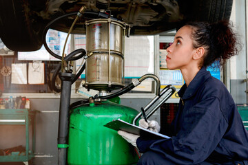 Wall Mural - Beautiful female auto mechanic checking wheel tires in garage, car service technician woman repairing customer car at automobile service, inspecting vehicle underbody and suspension engine system.