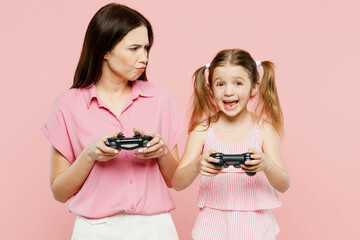 Wall Mural - Happy sad fun woman wear casual clothes with child kid girl 6-7 years old. Mother daughter hold play pc game with joystick console isolated on plain pastel pink background. Family parent day concept.