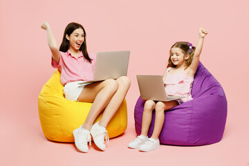 Wall Mural - Full body IT woman wear casual clothes with child kid girl 6-7 years old. Mother daughter sit in bag chair work hold use laptop pc computer isolated on plain pink background Family parent day concept.