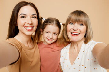 Wall Mural - Close up happy women wear casual clothes with child kid girl 6-7 years old. Granny mother daughter do selfie shot pov on mobile cell phone isolated on plain beige background. Family parent day concept