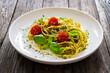 Noodles with basil pesto, parmesan cheese, tomatoes and basil leaves served on wooden table 