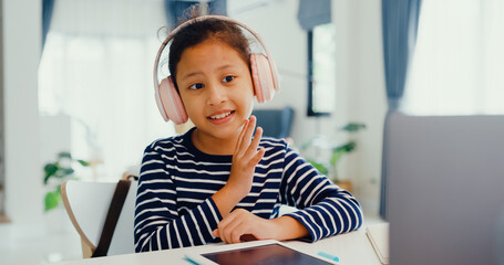 Asian toddler girl with sweater wear headphone sit front of desk with notepad use magic pen focus on writing do homework, finger counting number math online learning course from laptop at home.
