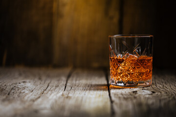A glass of Whiskey on a rustic wooden board, that can be surface of barrel. Moody atmosphere.