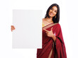 Cheerful Indian woman in traditional saree holding and pointing sign board isolated on white. advertisement concept. 