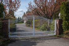Iron Front Gate Of A Luxury Home With Beautiful Garden. Wrought Iron White Gate And Brick Pillar