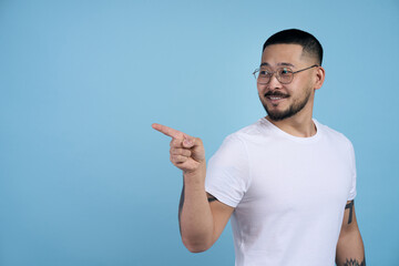 Wall Mural - Smiling asian bearded man pointing to side copy space with one hand