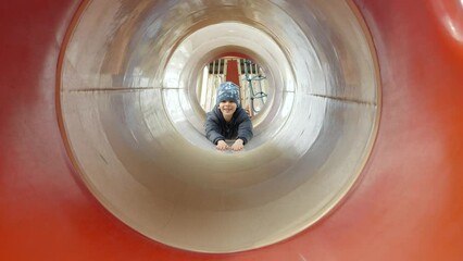 Wall Mural - Portrait of cheerful smiling boy riding down the slide on stomach. Happy kids, fun outdoors, leisure in park