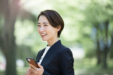 Poster - 逆光の中スーツを着たスマホで話す女性　ビジネスの転職・採用・女性起用などに