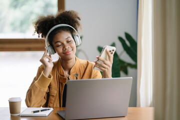 Smiling girl relaxing at home, she is playing music using smartphone tablet, laptop, and wearing white headphones.