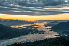 High-angle View Of The Mekong River Flowing Through Laos And Thailand. The Top Of The Mountain Has Morning Fog Covering The Sky As The Sun Rises