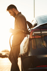 In the beautiful sunlight. Man is standing near his electric car outdoors