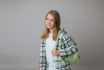 cheerful teenage girl 11,12,13 years old in a school uniform wears a backpack on a gray background. school fashion